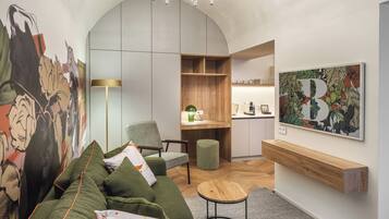 A modern living room with a green sofa, a small round table, and a kitchen area visible through an open doorway.