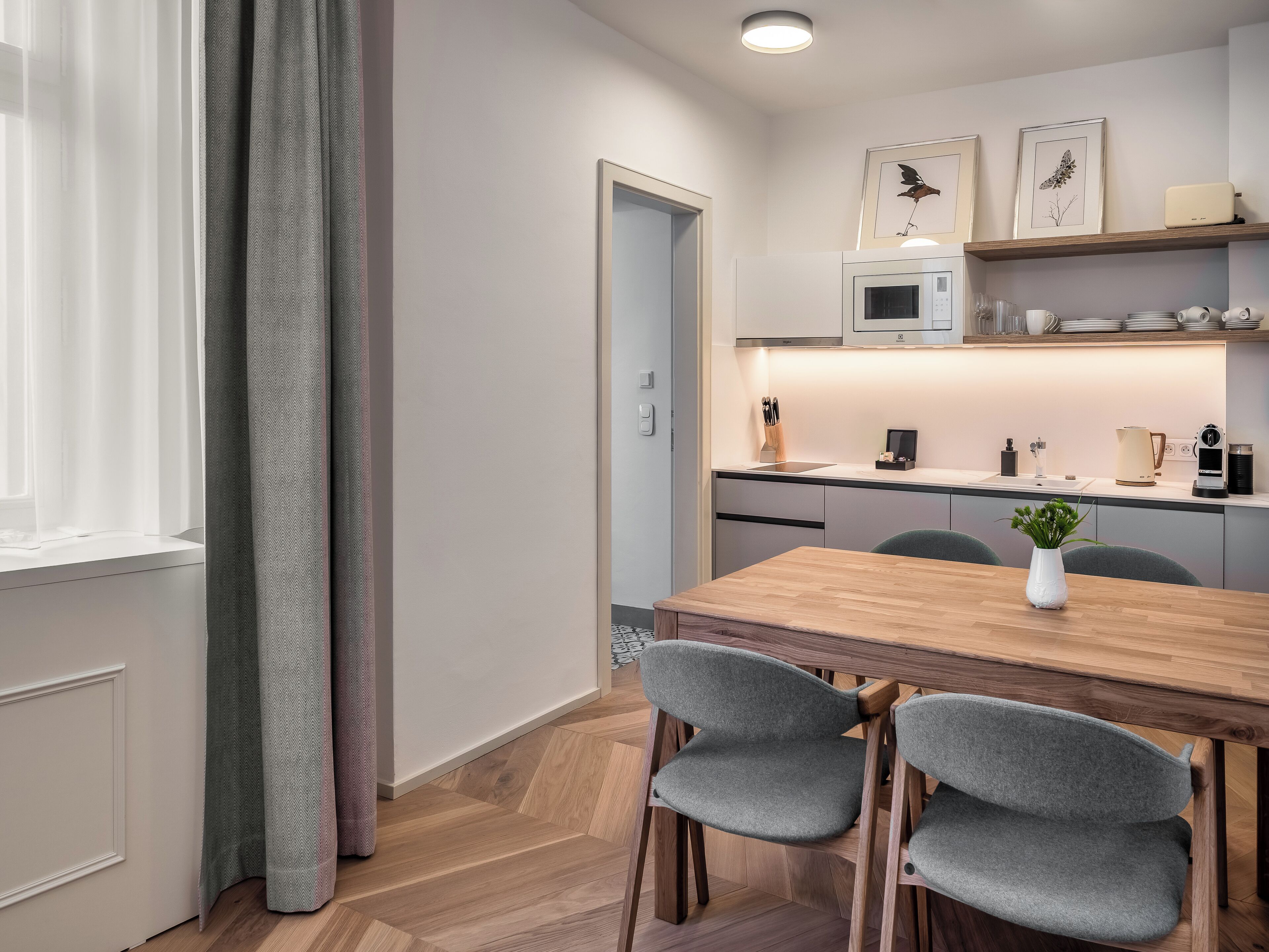 Una cocina moderna con una mesa de madera y sillas grises, un microondas y una cafetera.