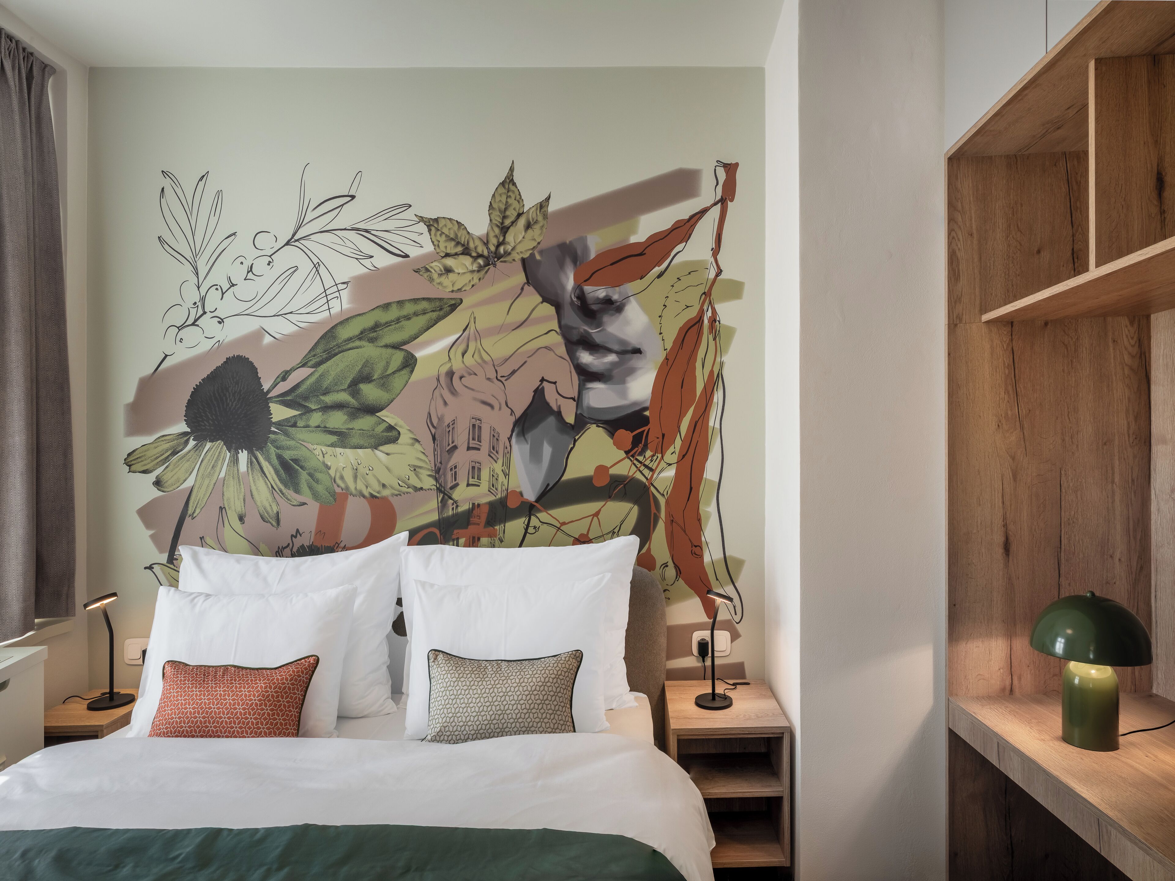 Una habitación de hotel con una cama, almohadas, una mesita de noche, una lámpara y un mural en la pared.