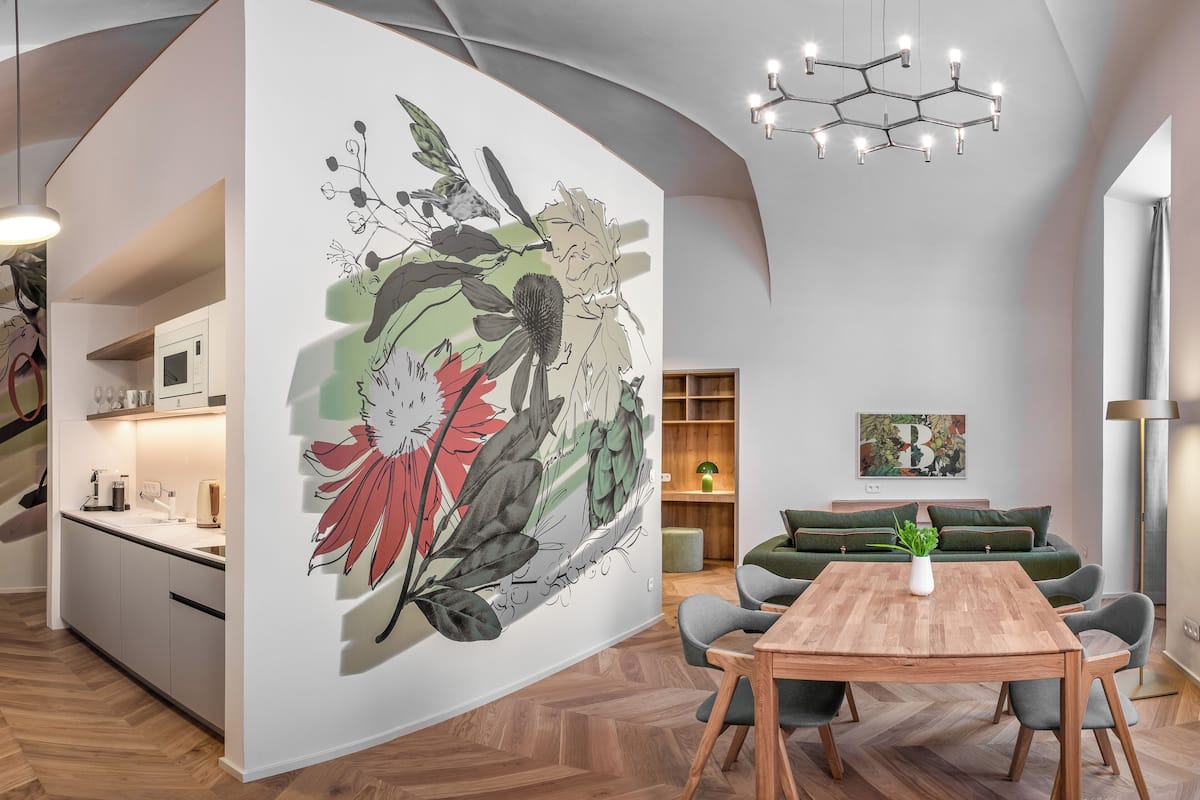 A modern interior with a wooden herringbone floor, a dining table with chairs, a green sofa, and a wall with a floral mural.
