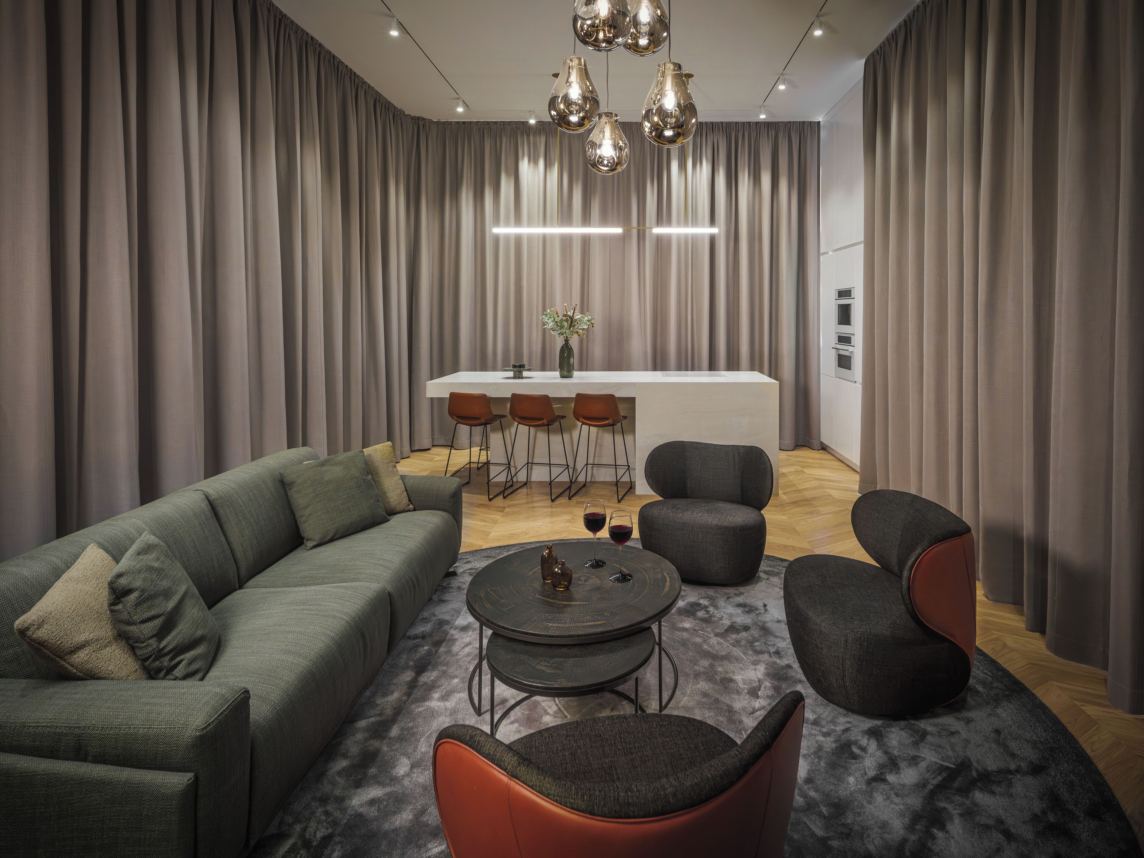Un salon moderne comprenant un canapé, des fauteuils, une table basse et un coin repas avec un bar.
