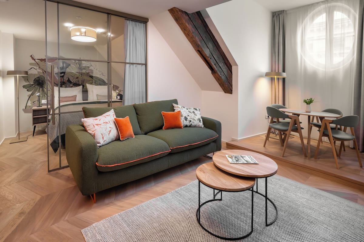 A modern living room with a green sofa, two round wooden tables, and a dining area with four chairs.