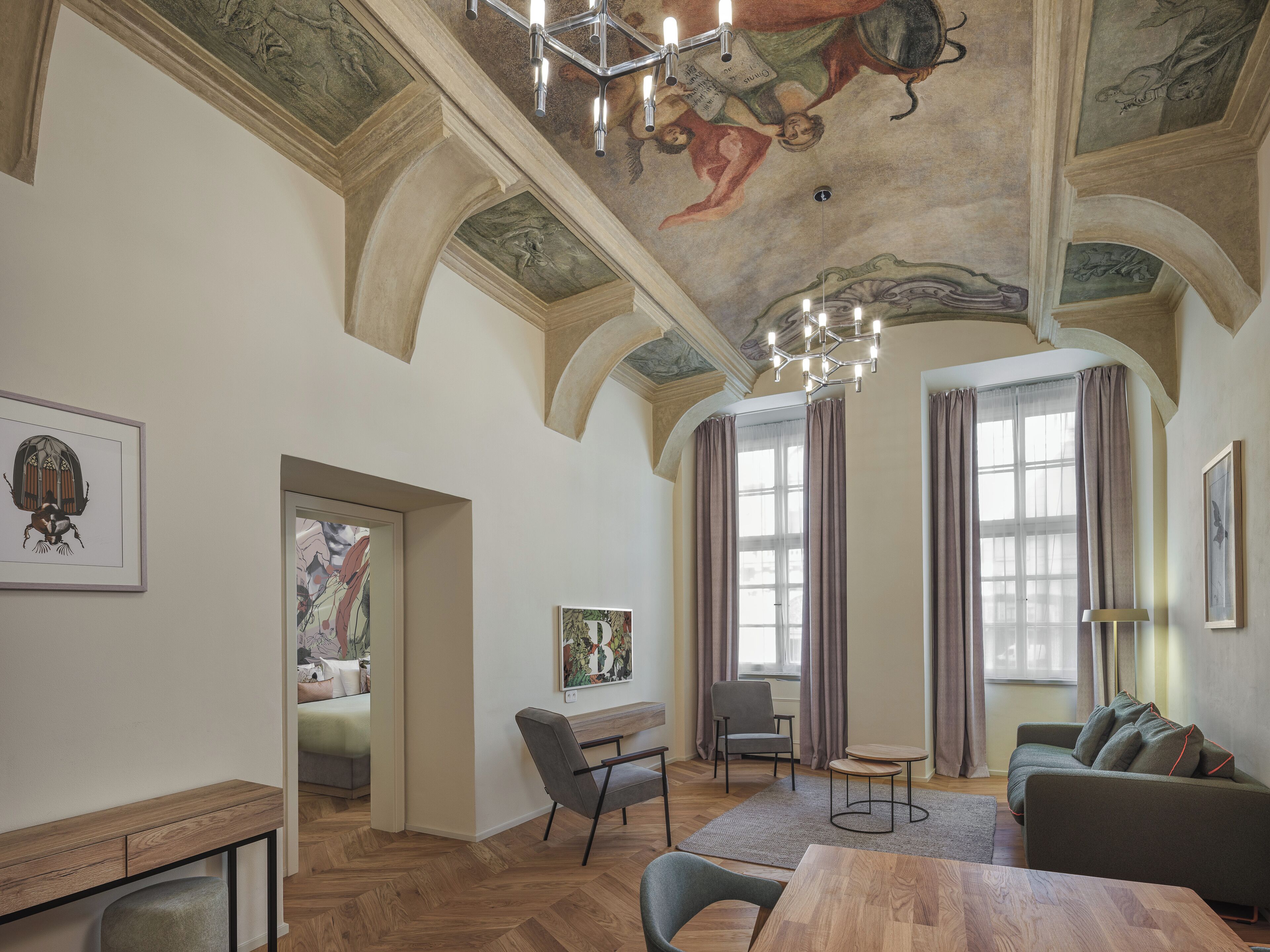 Ein geräumiger Raum mit hoher Decke, einer Kristallleuchtre, einem Sofa, einem Sessel, einem kleinen Tisch und einem Gemälde an der Wand.