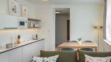 Cocina moderna con microondas, tostadora y cafetera. Hay un comedor con mesa y sillas.