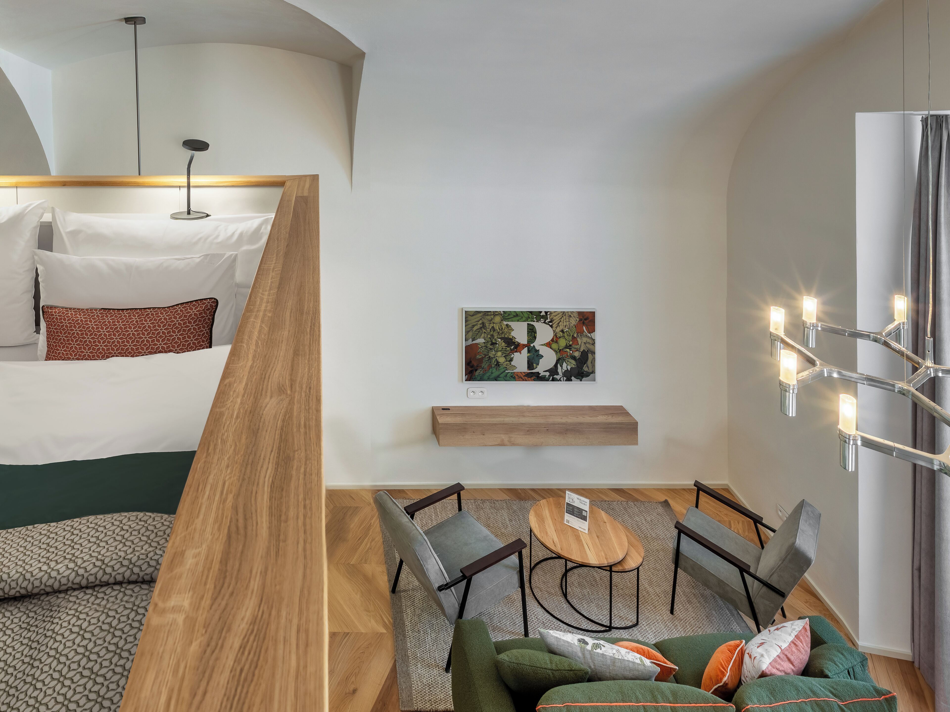 Una habitación de hotel moderna con cama, una mesita de madera, dos sillas, un sofá y una araña.