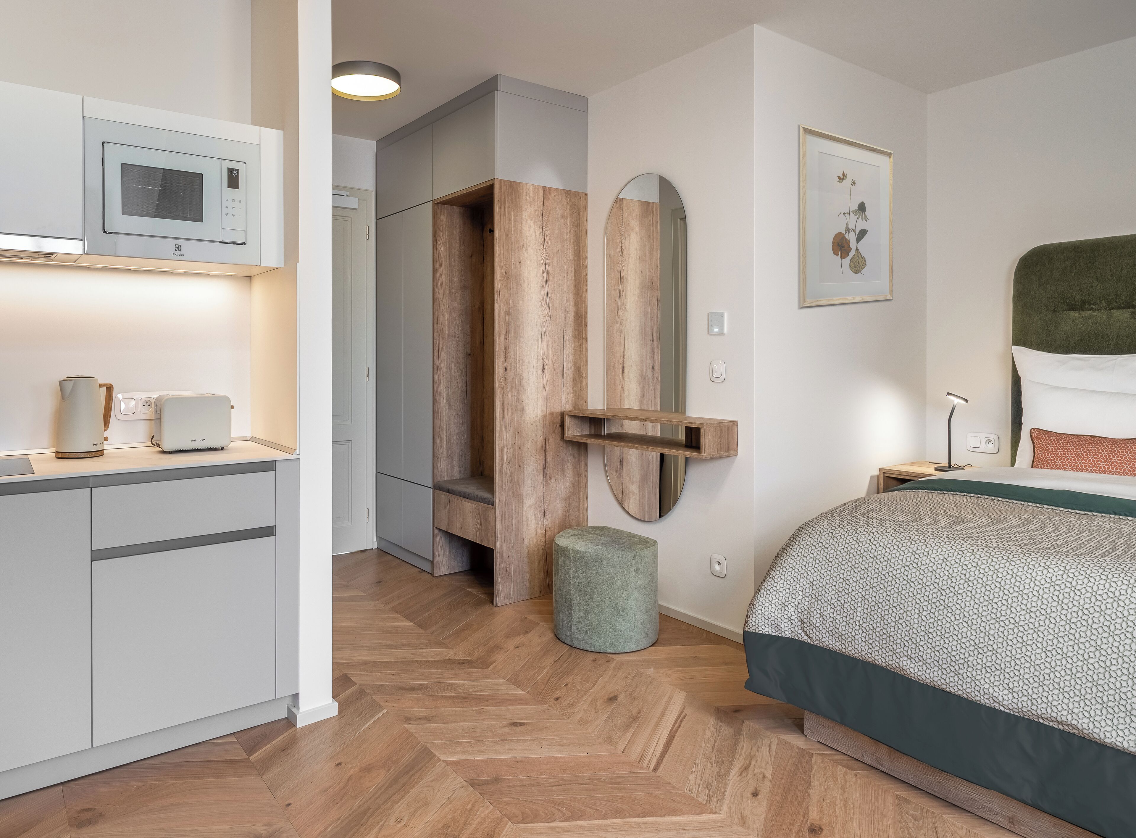 Una habitación de hotel moderna con kitchenette, una cama con colcha estampada, un panel de pared de madera y una obra de arte enmarcada.