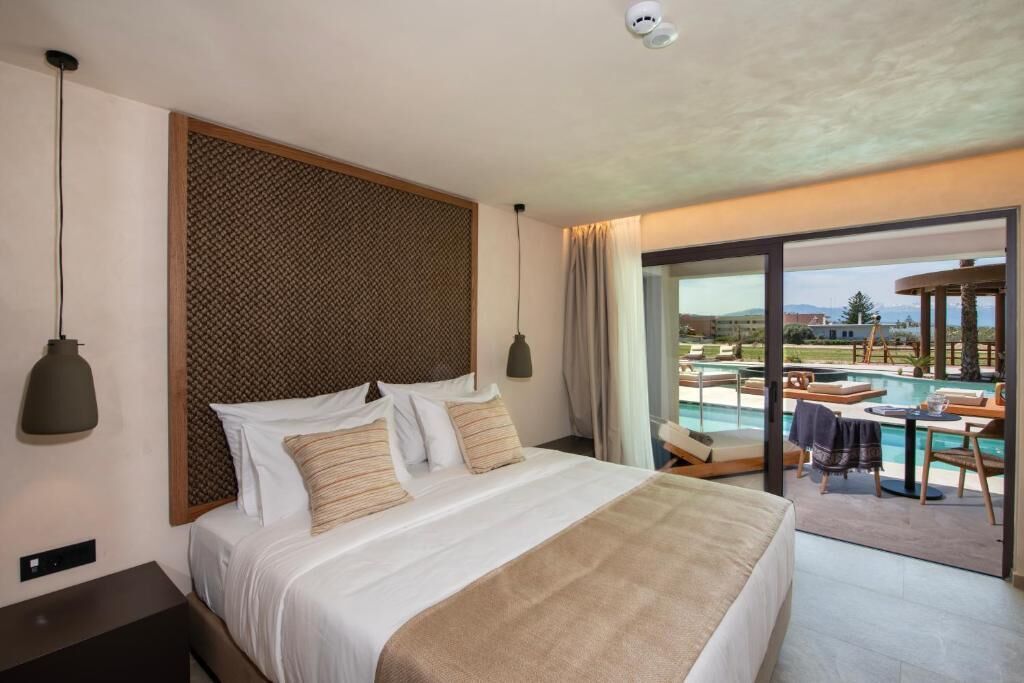 A hotel room with a large bed, a view of a pool and outdoor seating, and a ceiling-mounted light fixture.