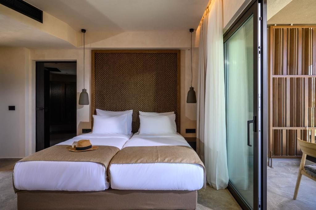 A double bed with a hat on the headboard, a large window with curtains, and a wooden panel wall.