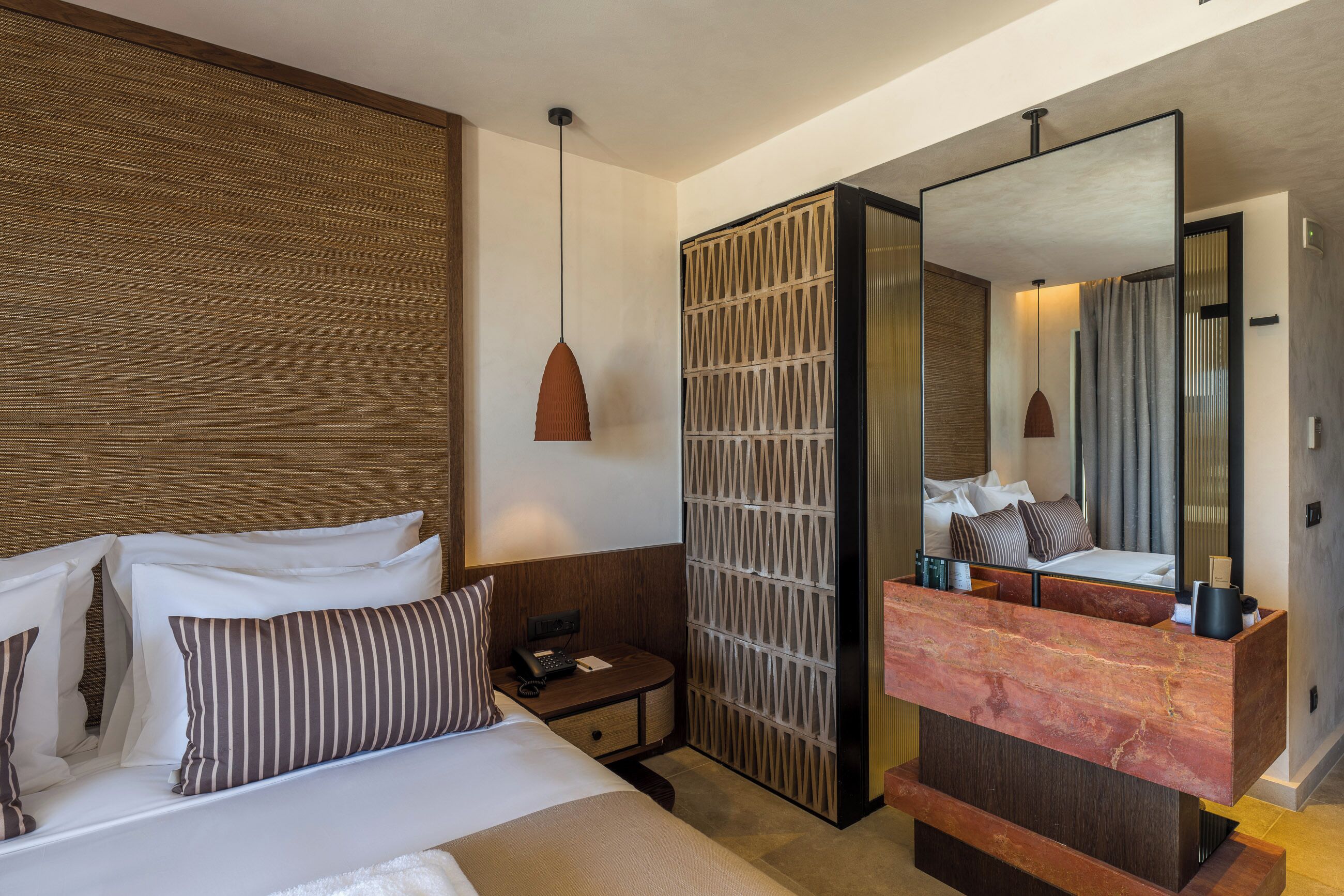Habitación de hotel con cama, mesita de noche, lámpara y un espejo grande.
