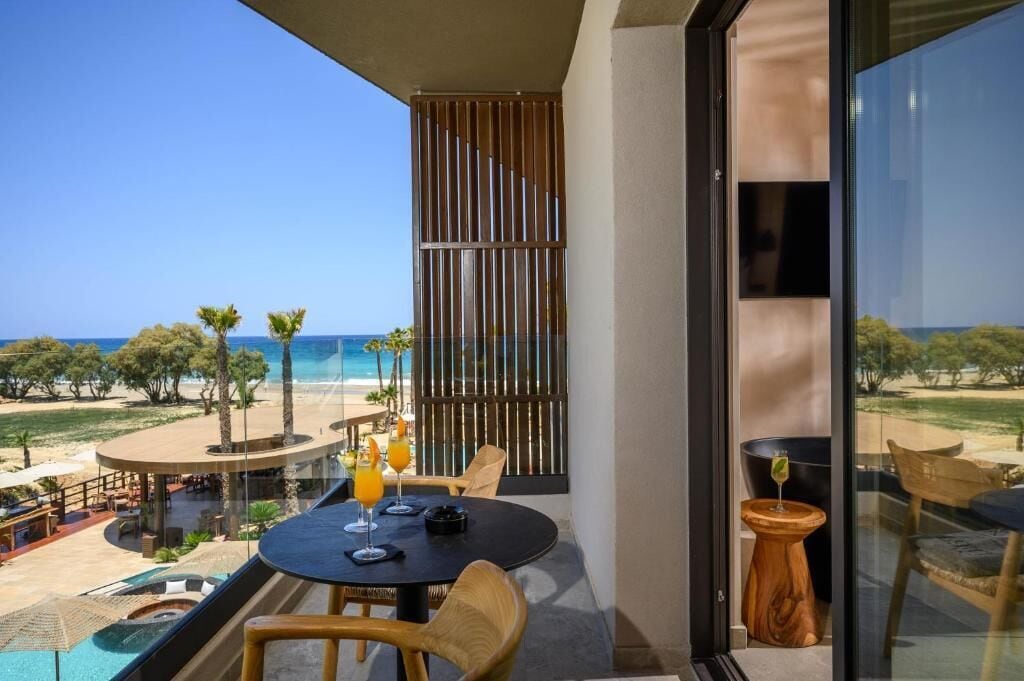 Un balcón con vistas a la playa, una mesa con bebidas y una piscina.