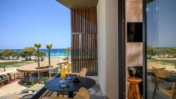 Un balcón con vistas a la playa, una mesa con bebidas y una piscina.