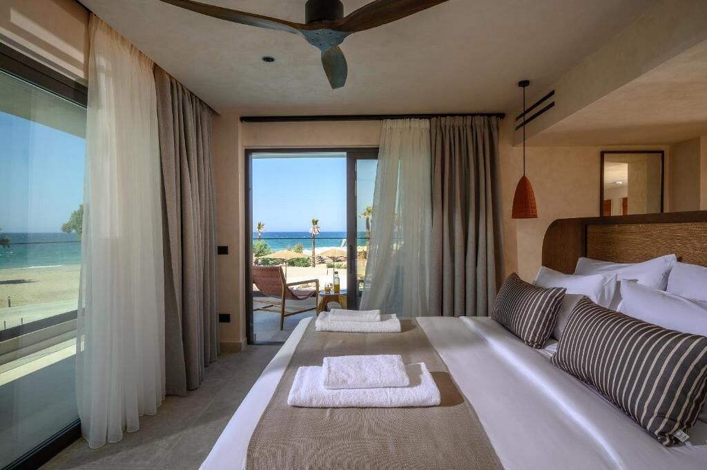 A hotel room with a bed, a view of the beach, and a balcony with a chair.