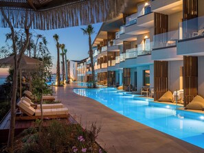 A modern hotel with a pool, palm trees, and lounge chairs. - Nalu Resort & Spa (Rethymno)