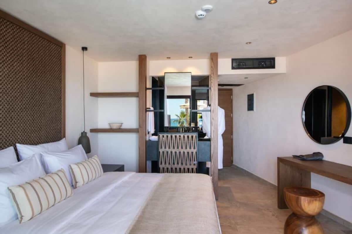 Une chambre d’hôtel moderne avec un grand lit, une tête de lit en bois, un petit bureau et un miroir.