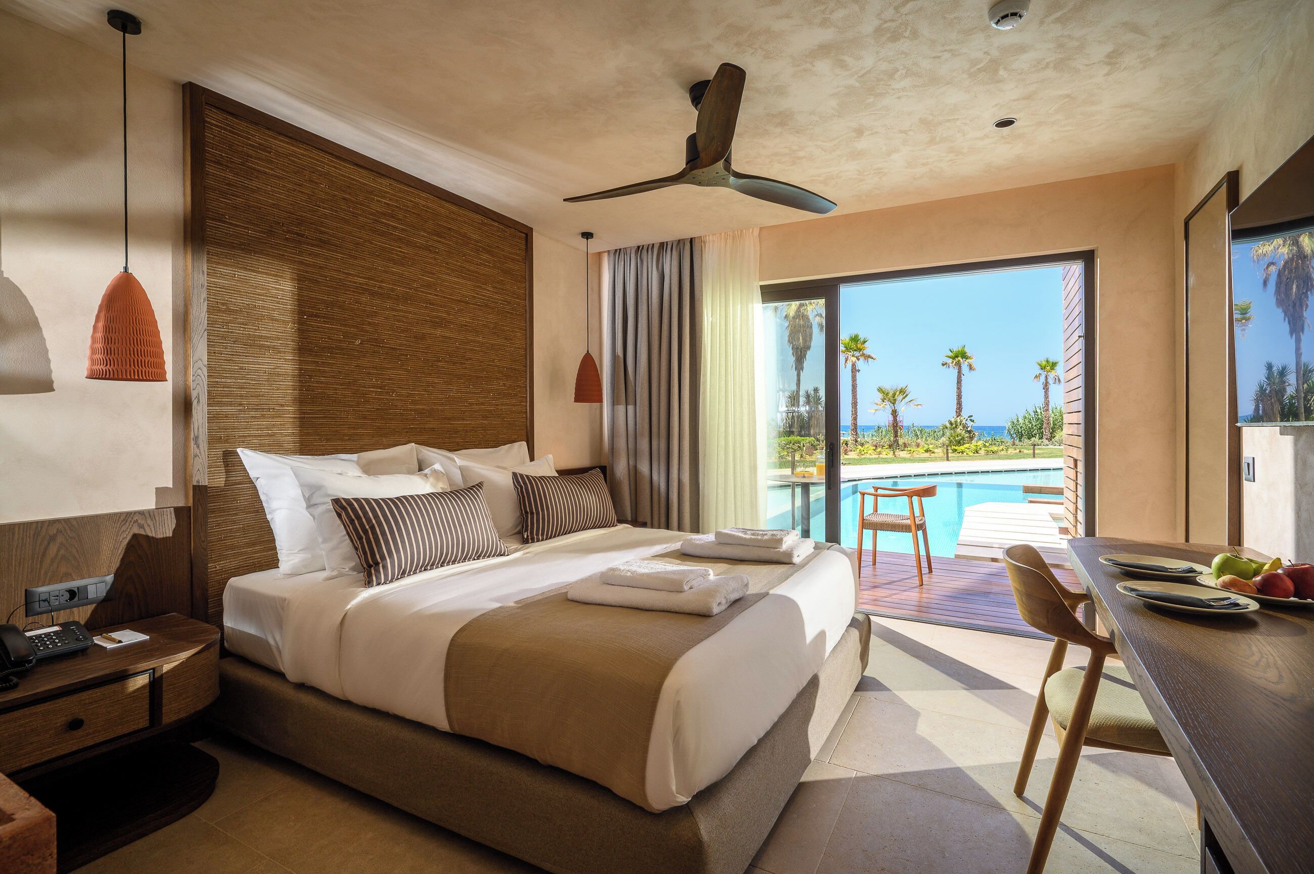 A hotel room with a bed, a desk, a chair, a pool view, and a ceiling fan.