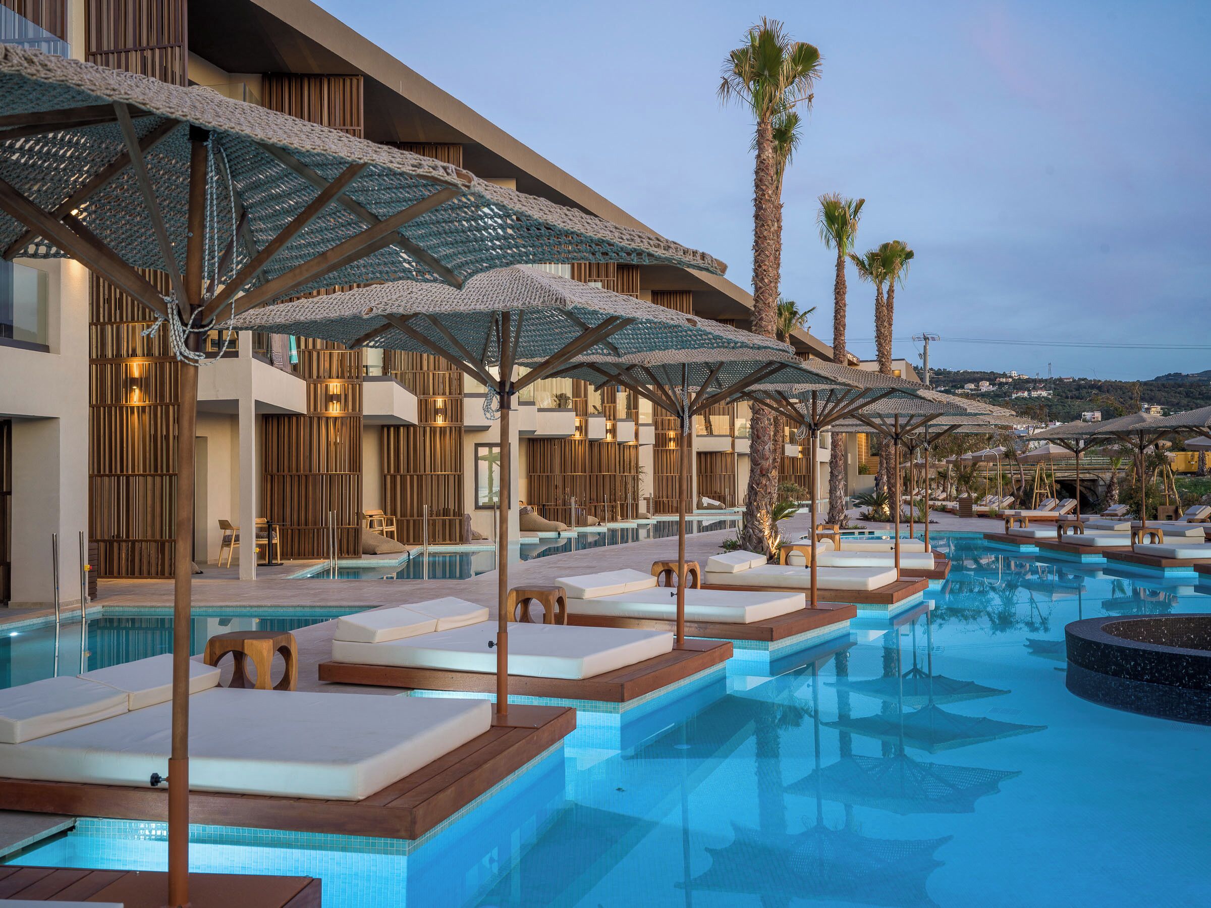 A poolside area with lounge chairs and umbrellas, a pool, and a building with wooden paneling and balconies.