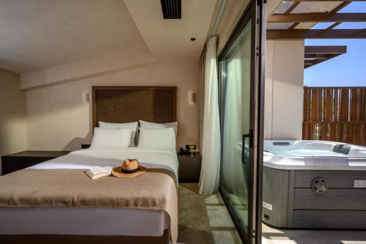 Une chambre d’hôtel avec un lit, une table de chevet, une lampe de lecture, un chapeau et un jacuzzi.