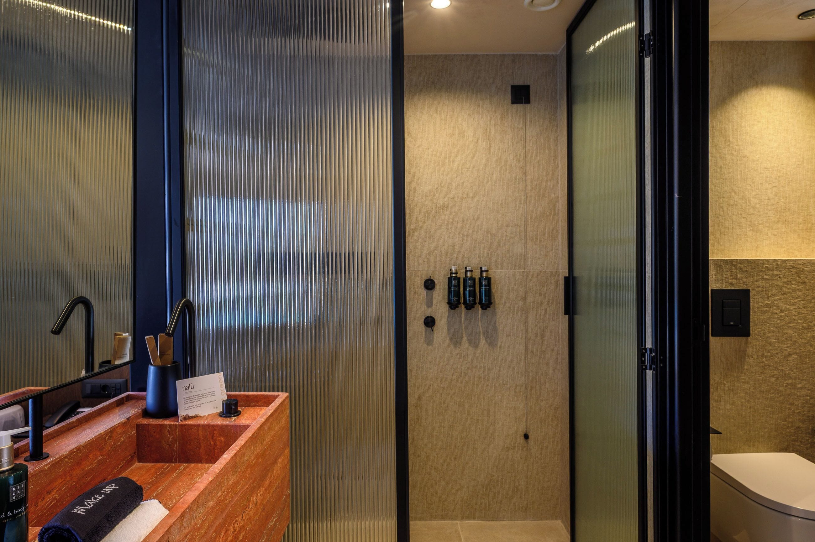 Een moderne badkamer met een houten wastafelmeubel, een glazen douchecabine en een beige wand met structuur.