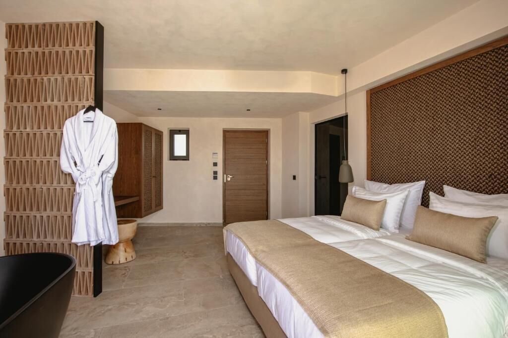 Una habitación de hotel moderna con una cama grande, cabecera de madera, una bata colgada en un perchero y una puerta de madera.