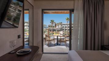 Habitación de hotel con cama, mesa de comedor con sillas, televisor montado en la pared y vista al área de la piscina del resort.