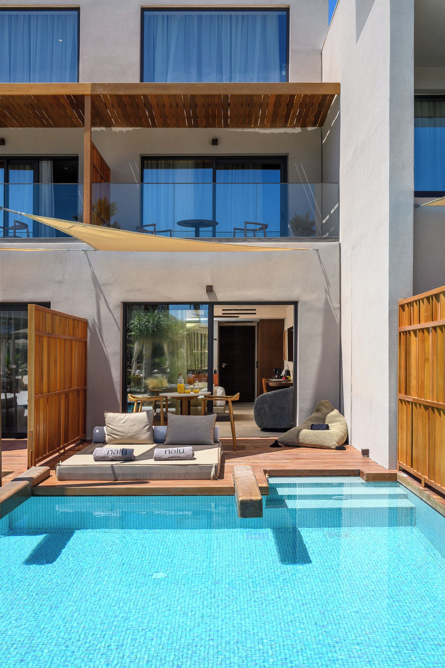 Un área de piscina moderna al aire libre con una silla de descanso, una mesita y una terraza de madera.