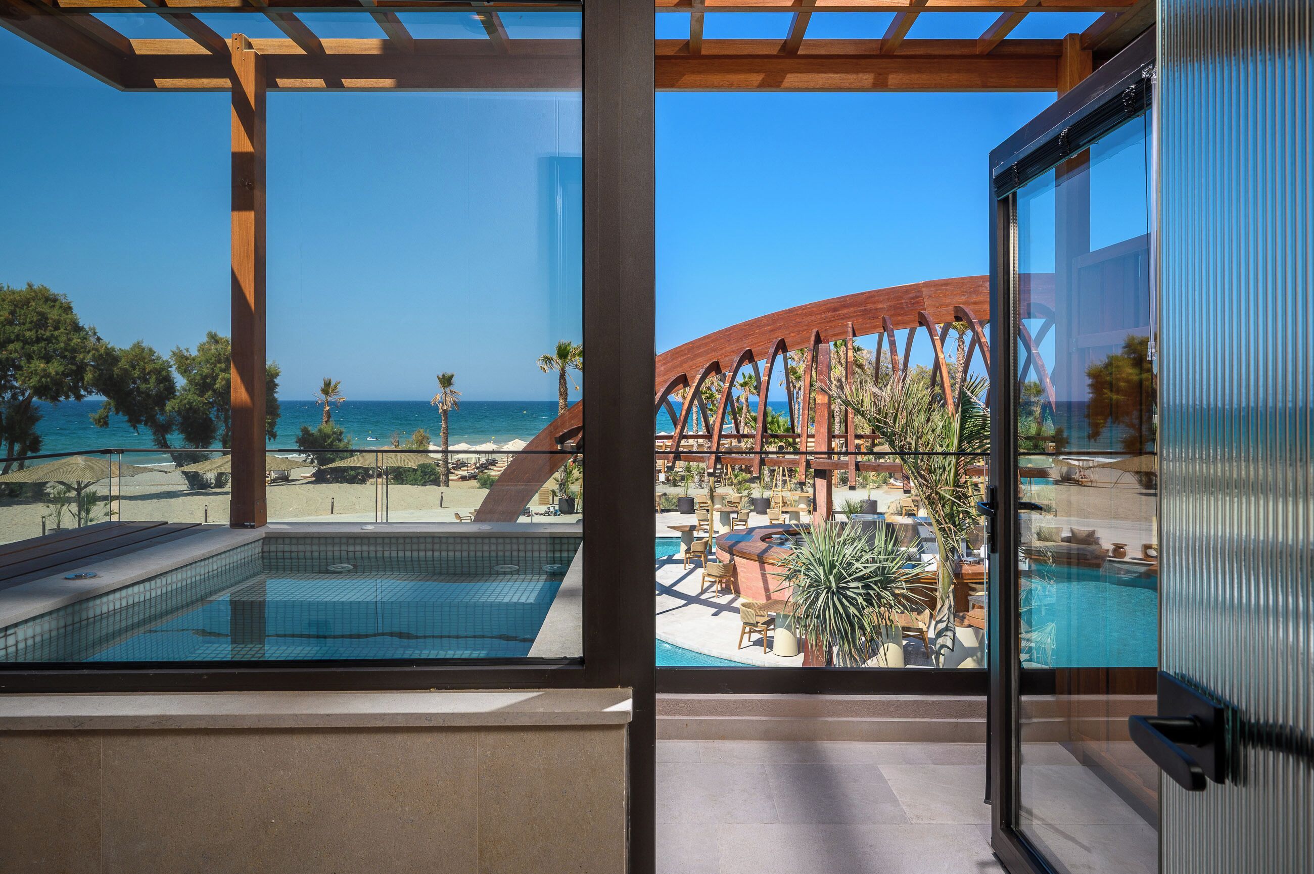 A balcony with a view of a pool, a beach, and a palm tree.