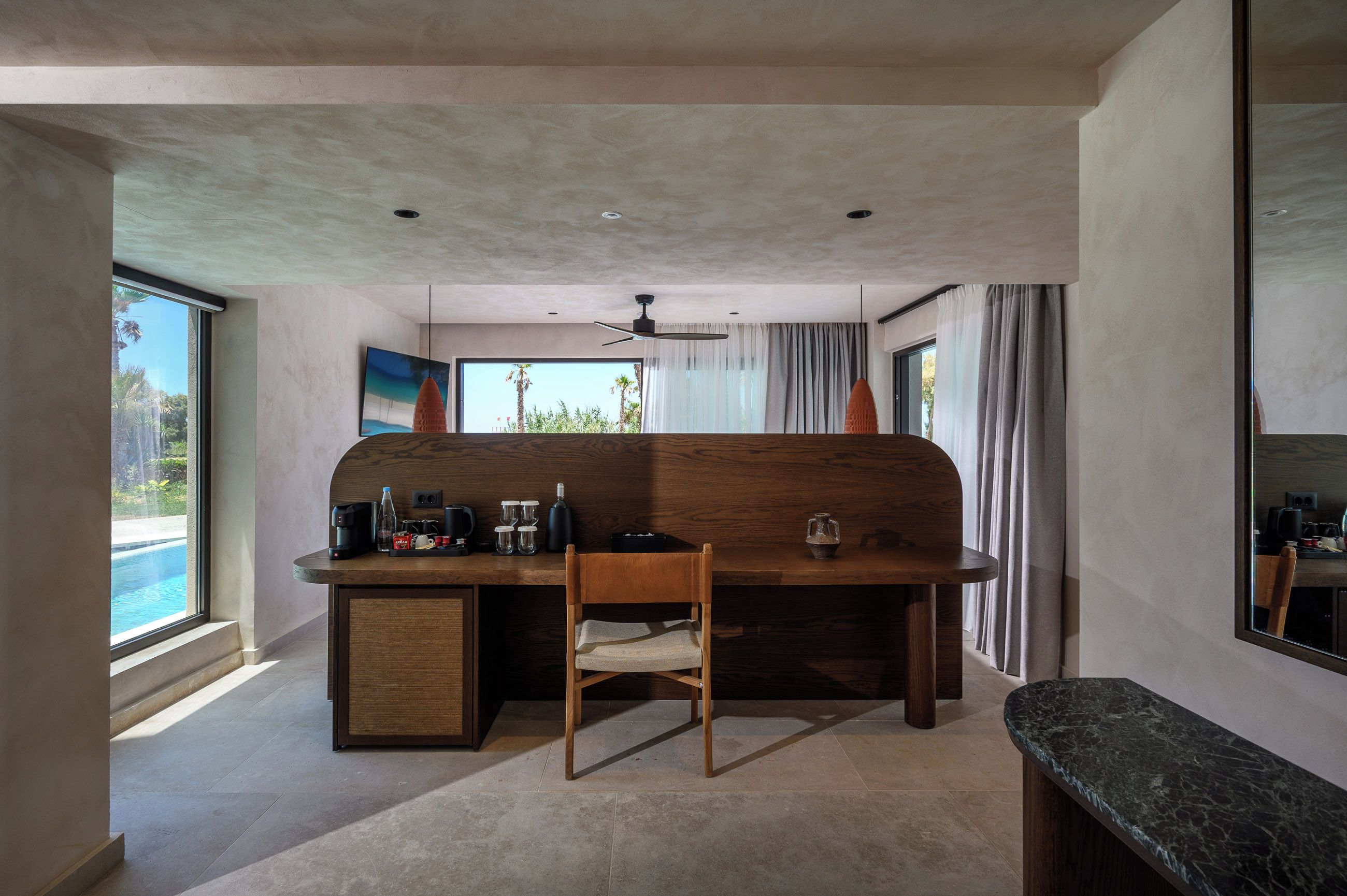 A modern kitchen with a wooden island, a dining area, and a large window with a view of palm trees.