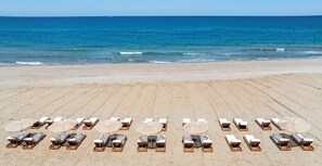 Ein Strand mit Reihen von Liegestühlen und Sonnenschirmen, der zum Meer hin ausgerichtet ist.