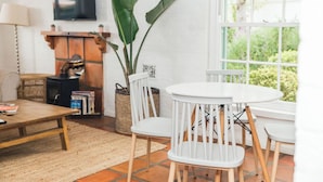 Un salon avec une cheminée, un téléviseur, une table ronde entourée de chaises et une grande fenêtre donnant sur un paysage verdoyant.