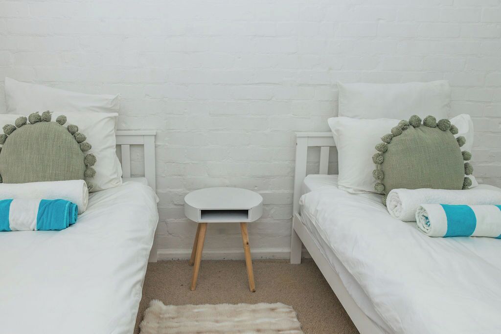 A room with two single beds, a small white side table, and a white brick wall.