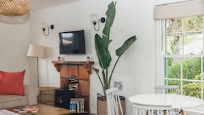 Un salon avec une cheminée, un téléviseur, une grande plante et une fenêtre donnant sur un paysage verdoyant.