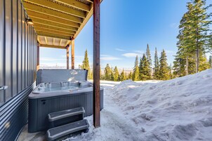 Un jacuzzi bajo una pérgola de madera, con un paisaje nevado y árboles de hoja perenne al fondo.