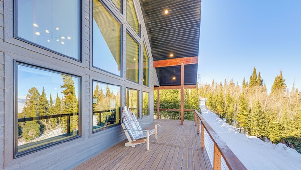 Ein modernes Gebäude mit großen Fenstern, einer Holzterrasse und Blick auf einen verschneiten Wald.