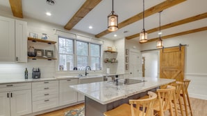 Une cuisine moderne avec des meubles blancs, un grand îlot central, des tabourets de bar en bois et des luminaires suspendus.