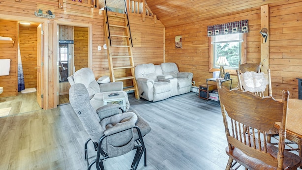 Et hyggeligt sommerhusinteriør med et loftsrum, en opholdsstue med sofa og stole, og et spisebord.