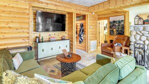 A cozy log cabin interior with a large TV, green sofas, a wooden cabinet, and a stone fireplace. - Walk to Golf, Lake: Twain Harte Cabin w/ Fireplace (Twain Harte)