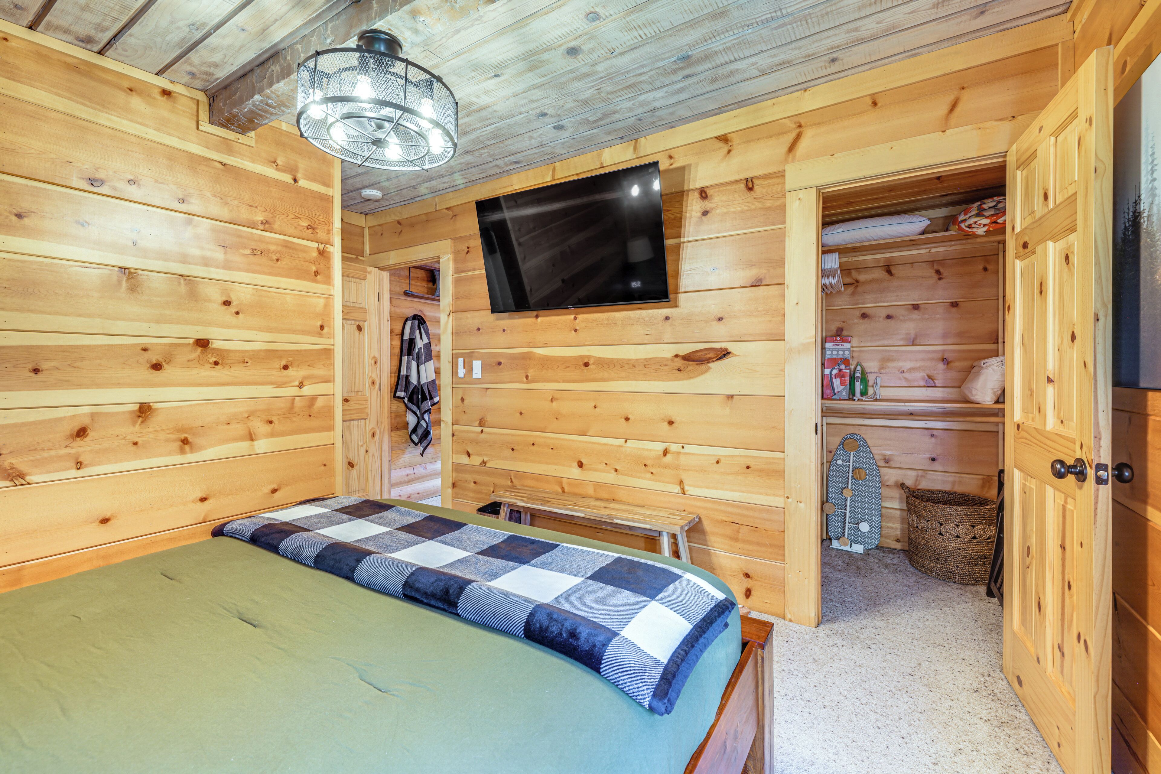 Una habitación de cabaña de madera con una cama, un televisor montado en la pared y un pequeño banco.