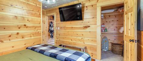 Una habitación de cabaña de madera con una cama, un televisor montado en la pared y un pequeño banco.