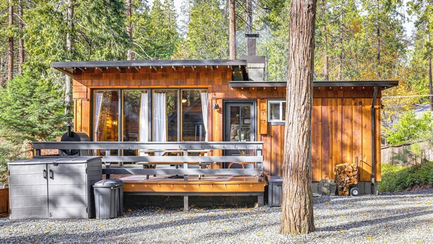 A cabin with a deck, a grill, and a large window overlooking a forest. - Walk to Golf, Lake: Twain Harte Cabin w/ Fireplace (Twain Harte)
