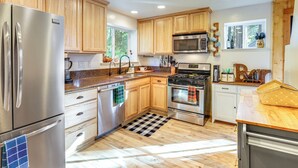 A modern kitchen with wooden cabinets, stainless steel appliances, and a checkered floor mat. - Walk to Golf, Lake: Twain Harte Cabin w/ Fireplace (Twain Harte)