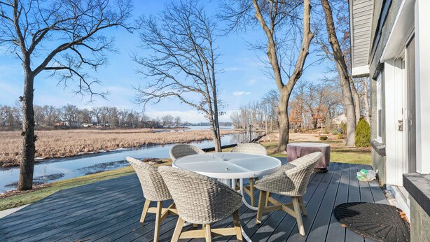 Eine Terrasse mit einem runden Tisch und Korbstühlen, mit Blick auf einen Fluss und Bäume.