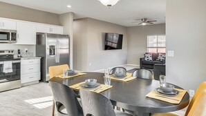 A modern kitchen with stainless steel appliances, a dining area with a dark table and chairs, and a ceiling fan. - 3 Mi to Tucson Mall: Home w/ Large Outdoor Space! (Tucson)