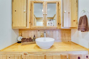 A wooden vanity with a large white basin, wooden cabinets, and a mirror.