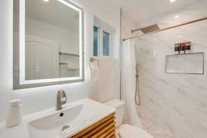 A modern bathroom with a white sink, a large mirror, a shower, and a marble wall.