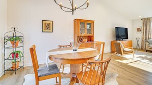 A dining area with a round wooden table, six chairs, a chandelier, a television, a cabinet, and a plant stand. - Deck w/ Forest Views: Modern Home in Rochester! (Rochester)