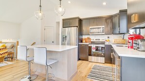 A modern kitchen with stainless steel appliances, a central island with bar stools, and a dining area with a wooden table and chairs. - Deck w/ Forest Views: Modern Home in Rochester! (Rochester)