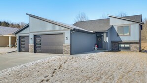 A two-story house with a garage, a front door with a wreath, and a stone accent wall. - Deck w/ Forest Views: Modern Home in Rochester! (Rochester)