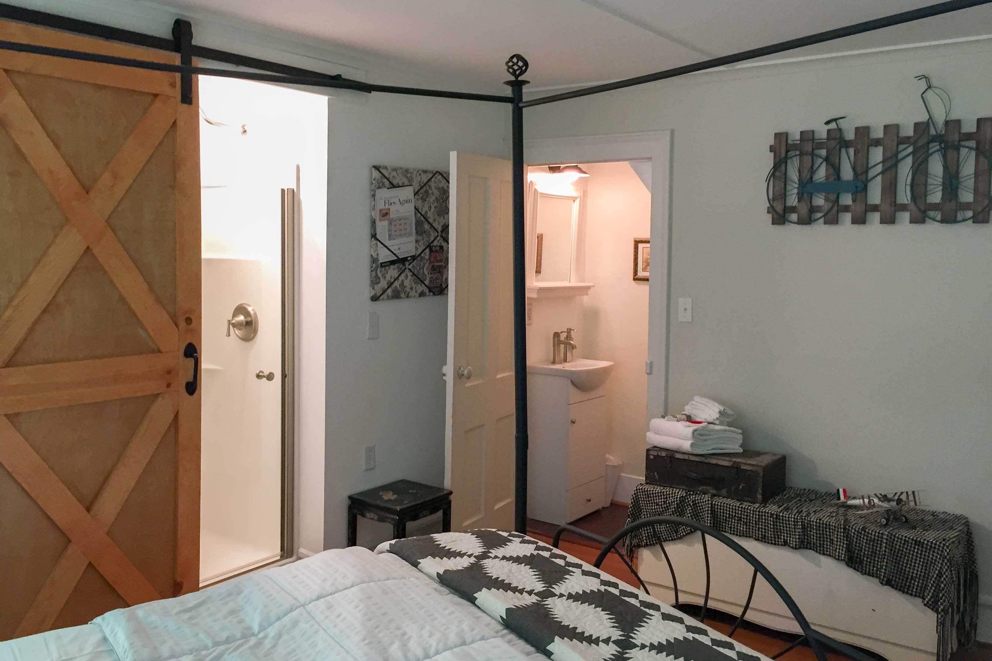 Un dormitorio con cama, cómoda, espejo y baño visible a través de una puerta abierta.