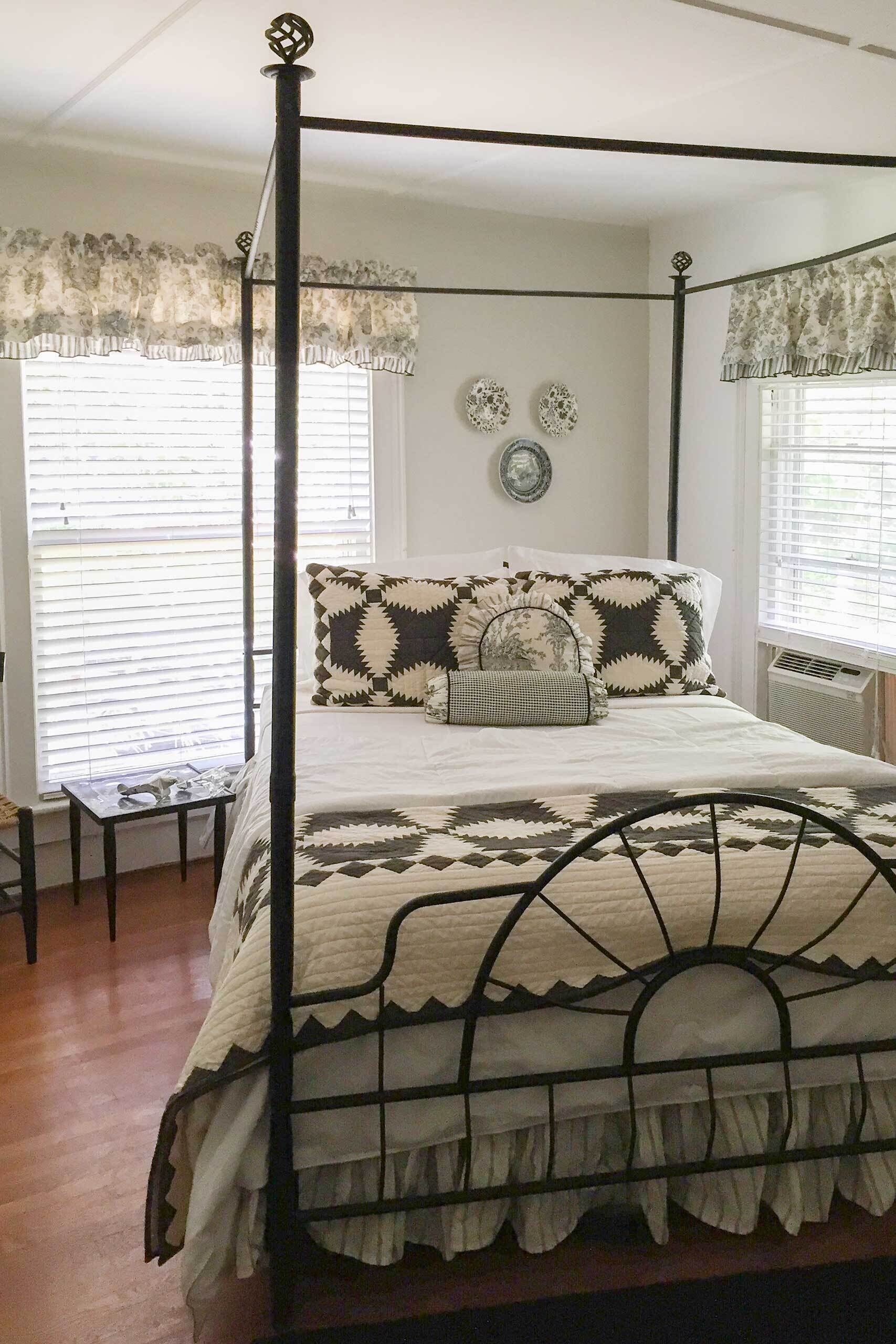 A four-poster bed with a white and black patterned bedspread, a small bedside table, and two wall decorations.