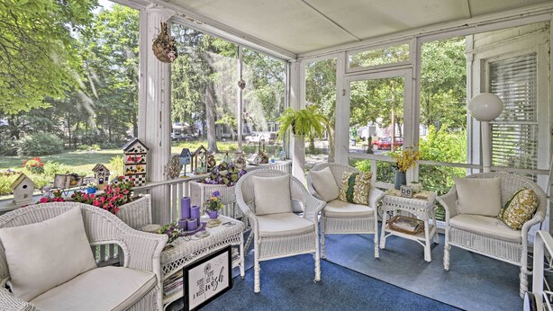 A sunlit porch with wicker furniture, a birdhouse collection, and a view of a lush garden. - Walk to Keuka Lake! Fun, Spacious Retreat w/ Pool (Hammondsport)